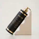 Um frasco de produto para cabelo preto e dourado de 500 ml da Lizzon 15 em 1 está apoiado em um ângulo em um suporte de pedra bege em forma de degrau contra um fundo branco liso.