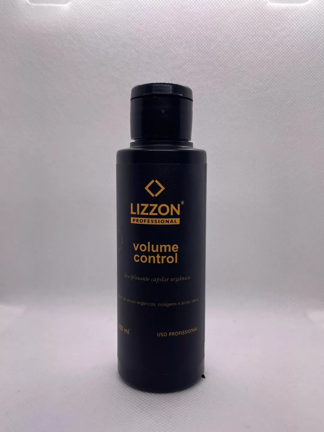 Um frasco preto de AMOSTRA VOLUME CONTROL rotulado com texto dourado, contendo 100 ml de alisante de cabelo liso orgânico, está na vertical contra um fundo cinza claro.
