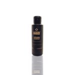 Um frasco preto com o rótulo "Amostra Volume Control - 100ml", com texto dourado e tampa preta, está na vertical sobre um fundo branco, com seu reflexo visível abaixo.