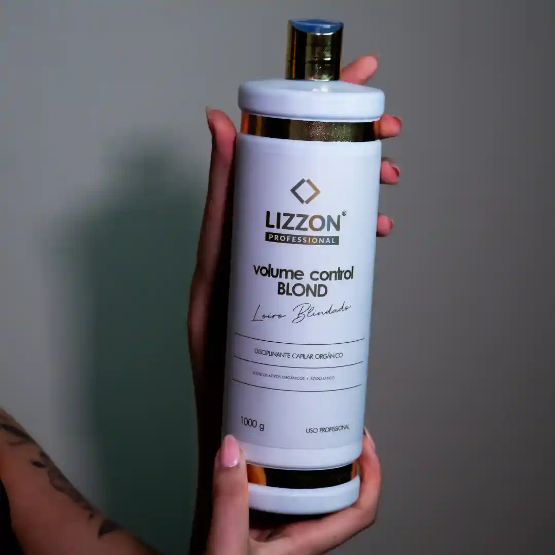 Uma pessoa segura um frasco branco grande do produto para cabelo Lizzon Professional Volume Control Blond com uma tampa dourada contra um fundo liso, mostrando a fórmula liso. O rótulo apresenta texto em preto e dourado com detalhes do produto.
