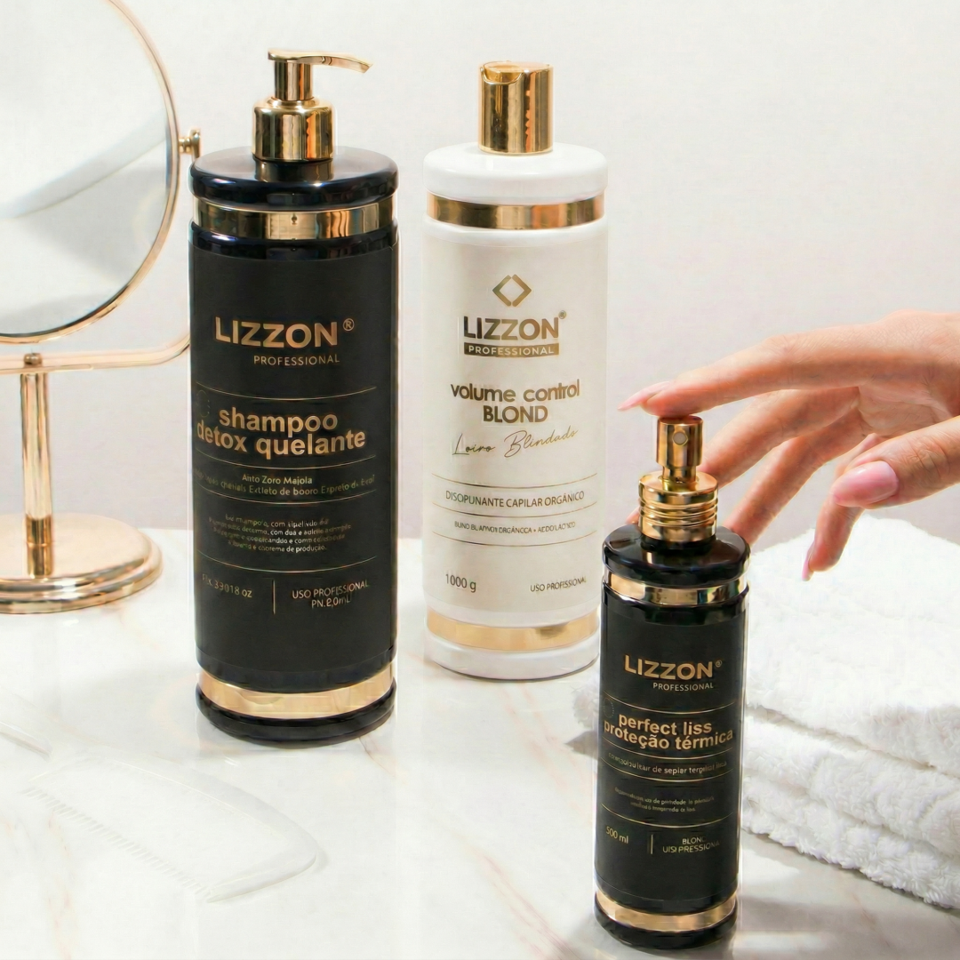 Três produtos de tratamento capilar Kit Liso Blindado Blond estão em uma bancada branca perto de um pequeno espelho redondo, com uma mão alcançando o frasco de spray preto e dourado.