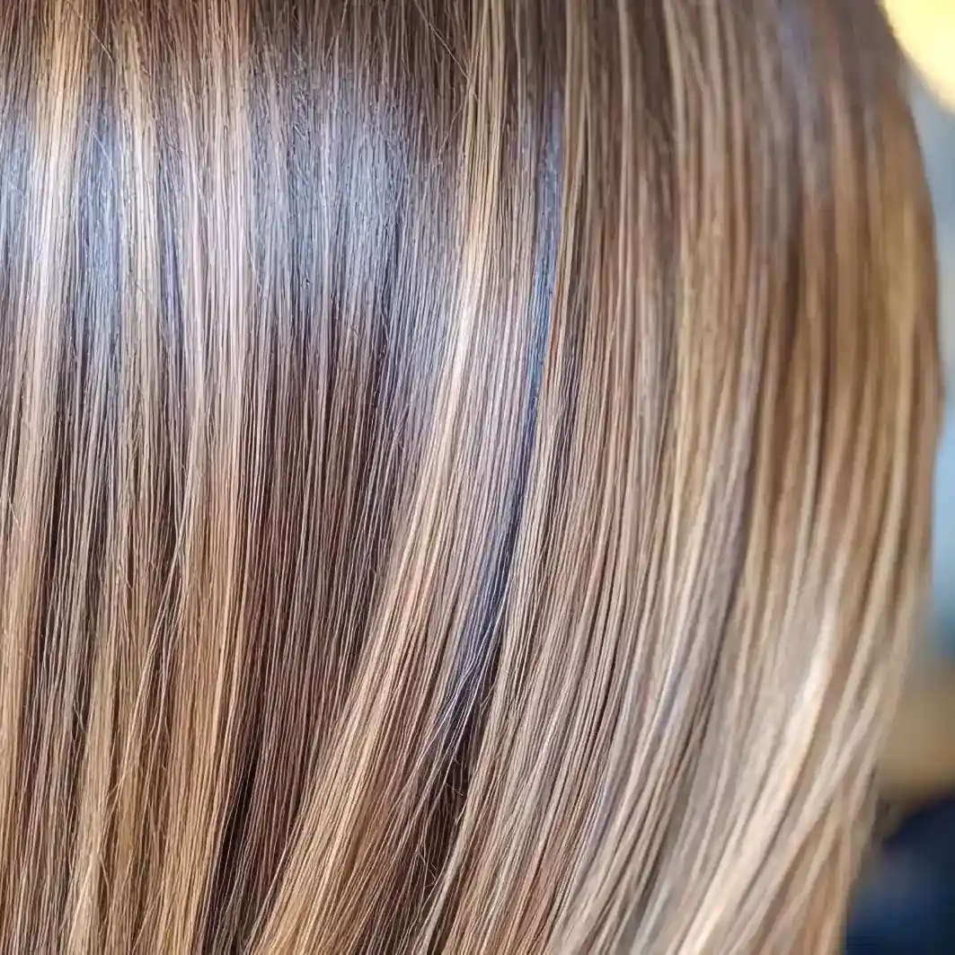 Close-up de cabelos lisos e brilhantes com mechas loiras e castanho-claras, exibindo textura suave, brilho saudável e controle especializado do volume usando o Volume Control Blond (embalagem 2unid black) para obter o visual loiro perfeito.