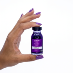 Uma mão com unhas pintadas de roxo segura um frasco de Power Dose Ampola Matização Blond Extreme de 15 ml com tampa e rótulo roxos, em um fundo branco.