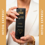 Uma pessoa de blazer branco e joias douradas segura uma caixa Retoq Express (Glow Express) com kit preto e dourado em um fundo combinado com o texto 