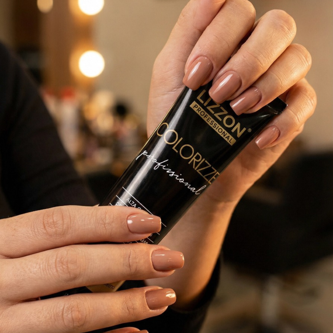 Uma pessoa com unhas nuas e bem cuidadas segura um tubo de Colorizze Coloração Creme Permanente, com um fundo interno desfocado.