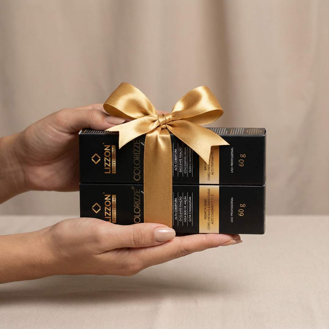 Duas mãos seguram duas caixas retangulares pretas empilhadas e amarradas com uma fita de cetim dourada. As caixas apresentam o nome do produto, 
