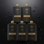 Cinco frascos pretos do Kit Emulsão Oxidante Colorimetria Express (5 unidades), cada um rotulado com 5, 10, 20, 30 e 40 volumes com detalhes em dourado, estão dispostos em uma superfície escura com gotículas de água.