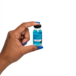 Uma mão com unhas pintadas de azul segura um pequeno frasco de líquido azul rotulado como Kit Power Dose em um fundo branco liso - ideal para a rotina do Kit Cronograma Blindado.