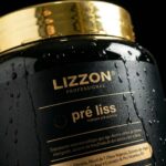 Um close-up de um recipiente preto e dourado com o rótulo Lizzon Professional pré liss máscara pré-química, com gotas de água na superfície. O rótulo inclui detalhes do produto em português.
