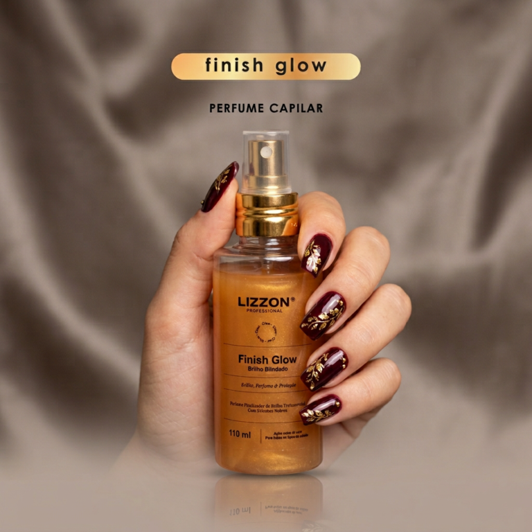 Uma mão com nail art em vermelho escuro e dourado segura um frasco de Lizzon Finish Glow Perfume Capilar em um fundo bege acetinado. O texto acima do frasco diz 