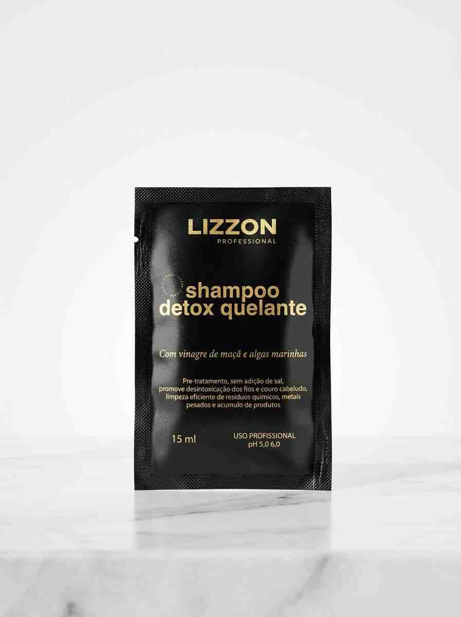 Um sachê preto com o rótulo "Amostra Shampoo Detox Quelante - 15 ml", com texto em dourado e branco, está na vertical em uma superfície de mármore branco contra um fundo branco liso.
