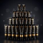 Uma pirâmide de tubos de Colorizze: Coloração Creme Permanente (combo 24 unidades) é exibida em um fundo escuro e suavemente iluminado, juntamente com OX Emulsão 20vol 900ml.