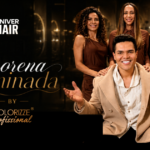 Quatro pessoas posam diante de um cenário escuro e elegante. Três mulheres estão em pé ao fundo, enquanto um homem sorridente está sentado à frente, com os braços abertos. O texto acima diz “Curso Coloração by Colorizze Professional” e “Univer Hair”.