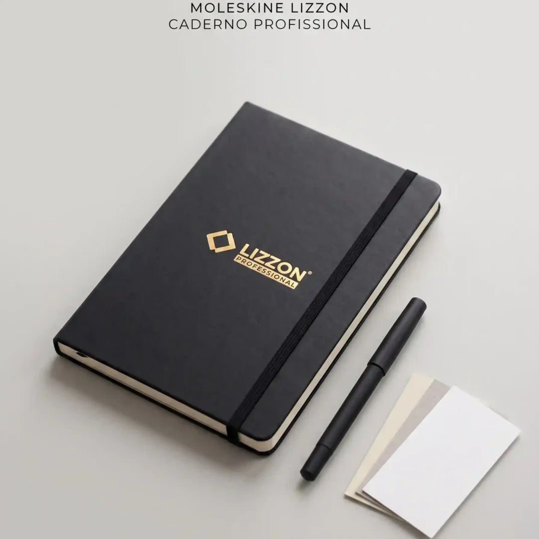 Um caderno profissional Lizzon preto com uma faixa elástica, uma caneta preta e dois cartões em branco estão dispostos sobre uma superfície cinza-clara. O texto acima diz: Moleskine Lizzon Caderno Profissional..