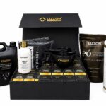 Uma caixa preta com a etiqueta “Kit Lizzon Express” contém diversos produtos para os cabelos, incluindo frascos, pacotes, uma tigela para misturar e sachês, todos com embalagens nas cores preta, dourada e branca. Os itens estão dispostos de forma organizada para exposição.