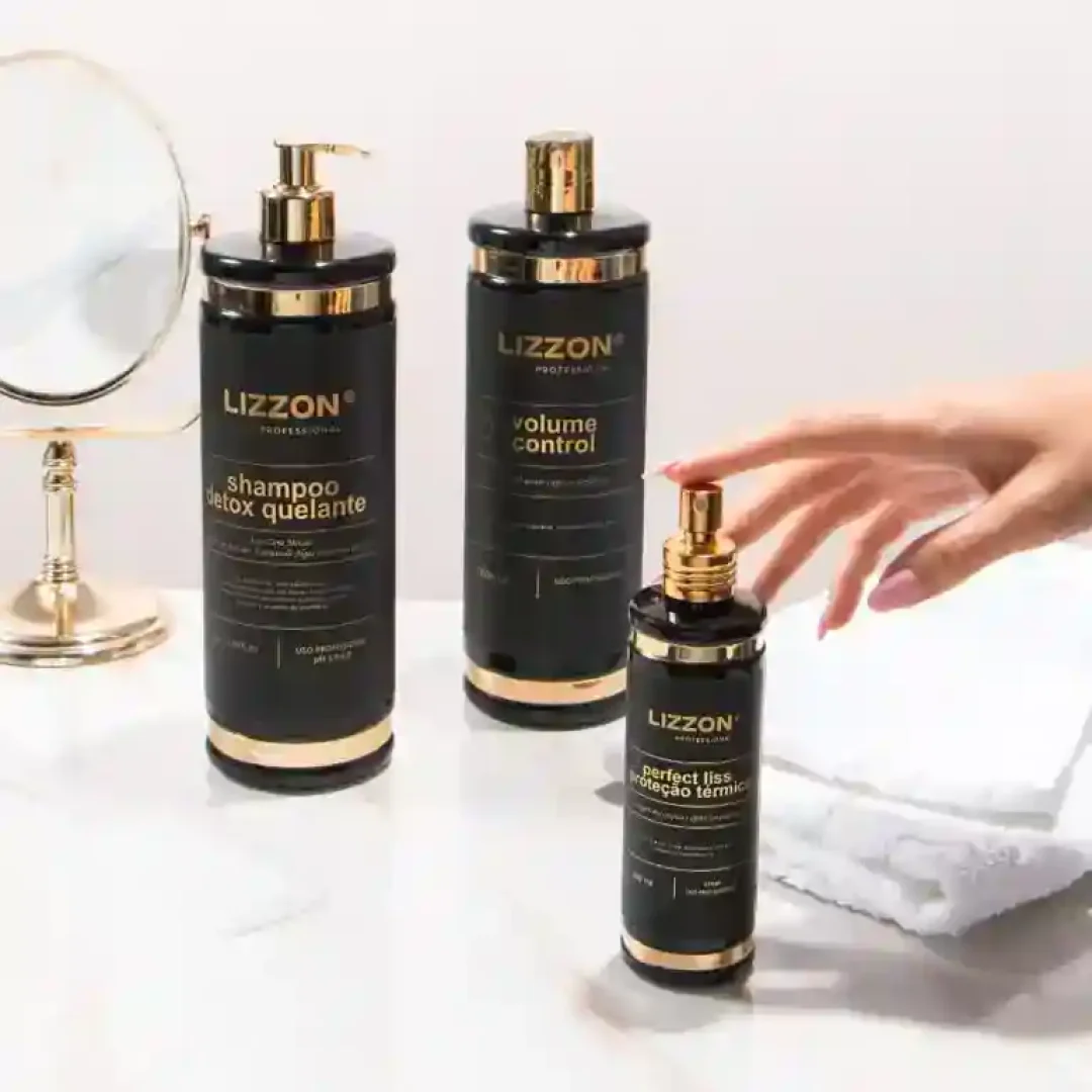 Três frascos pretos e dourados de produtos para cabelo da Lizzon estão em uma superfície branca, ao lado de uma toalha branca dobrada, um espelho redondo e uma mão pegando um frasco.